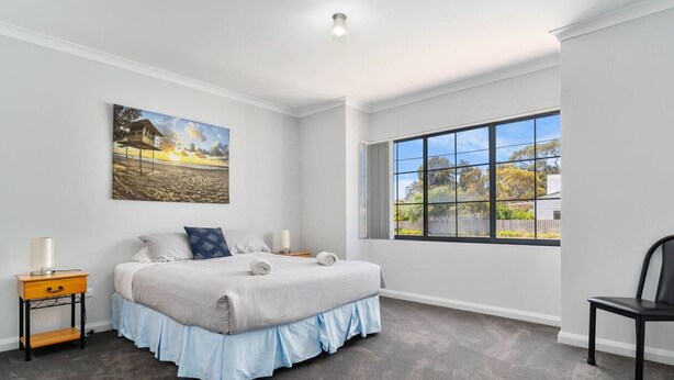A bedroom with a bed, a nightstand, a chair, a window with a view, and a painting on the wall. - Mandurah Estuary Breeze (Wannanup)