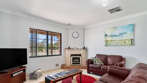 A living room with a fireplace, a television, a couch, and a large window. - Mandurah Estuary Breeze (Wannanup)