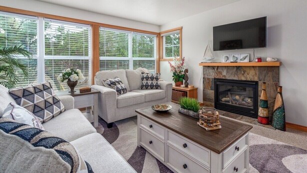 A living room with a fireplace, a sofa set, a coffee table, and a television mounted on the wall. - Seaside Paradise - lovely townhome, beach paths, dog OK (Pacific City)