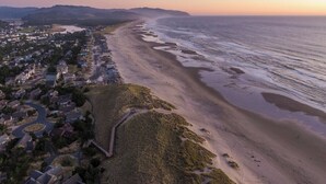 An aerial view of a coastal town with a beach, houses, and a winding road. - Seaside Paradise - lovely townhome, beach paths, dog OK (Pacific City)