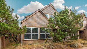 A two-story house with a sloped roof, large windows, and a wooden exterior. - Seaside Paradise - lovely townhome, beach paths, dog OK (Pacific City)