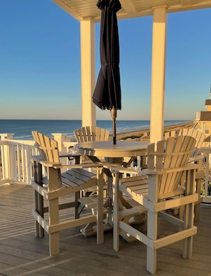 Een houten terras met een ronde tafel en stoelen, een parasol en uitzicht op de oceaan.