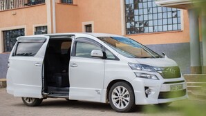 A white minivan parked in front of a building with a large window and a balcony.