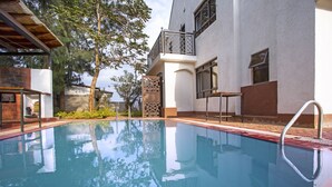 A swimming pool with a clear view of the surrounding architecture, including a modern building with a balcony and a wooden pergola.