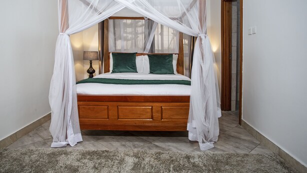 A bed with a wooden frame, white bedding, and green pillows, with a white canopy.