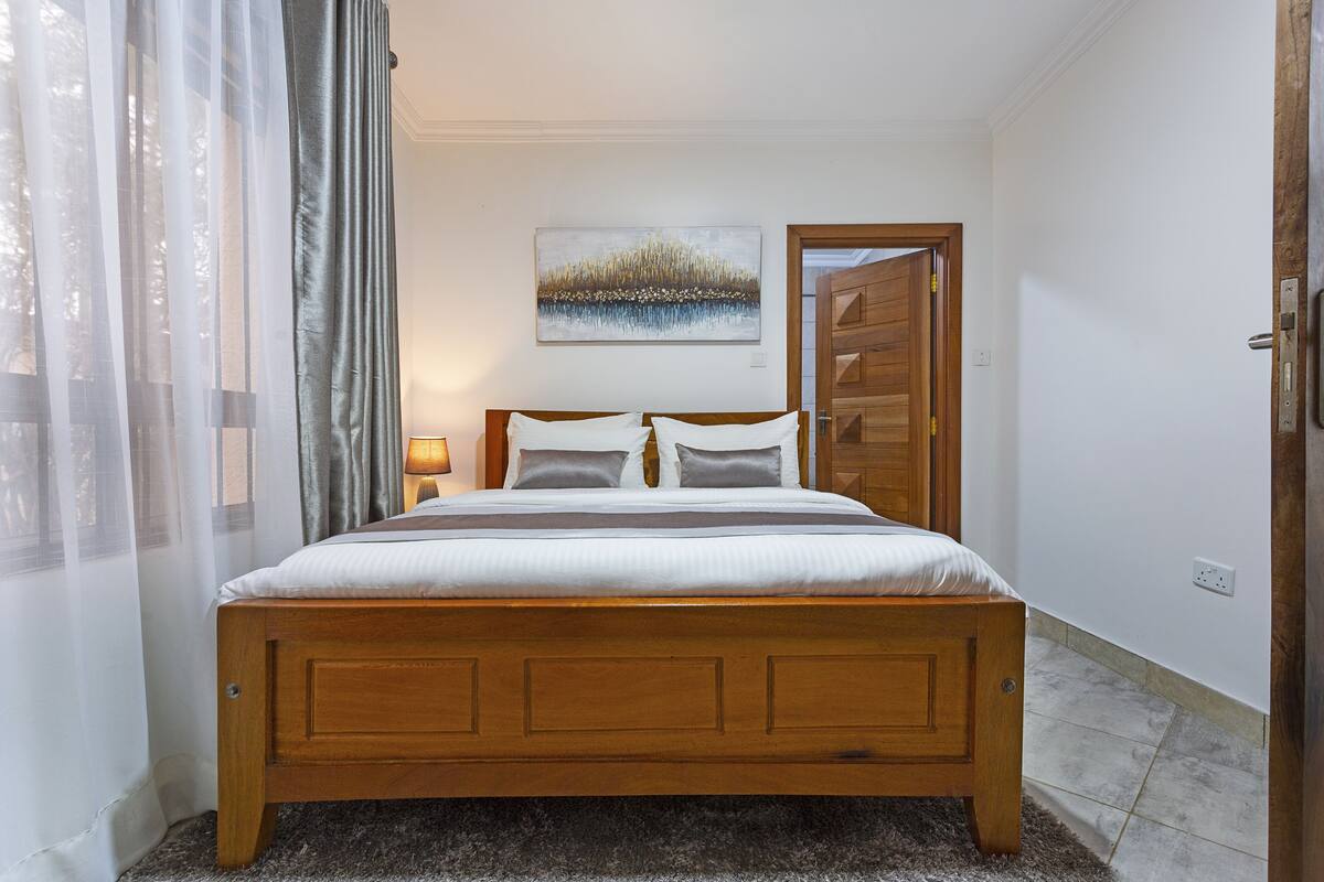A bedroom with a wooden bed, a painting on the wall, and a door leading to another room.