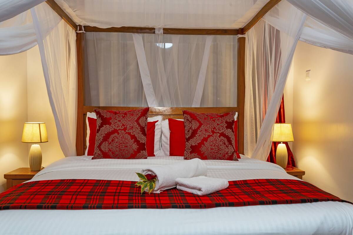 A bed with a red and black plaid bedspread, white bedding, and red and white patterned pillows. There are two bedside lamps on wooden nightstands.
