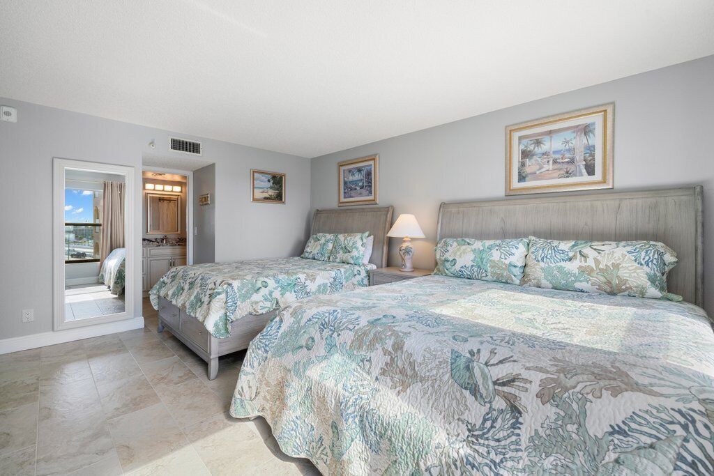 A bedroom with two beds, a bathroom, and a view of the outdoors.