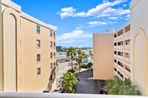A view from a balcony overlooking a parking lot with palm trees, a road, and buildings with balconies. - 2 Bedroom Condo With Drawbridge View (Madeira Beach)