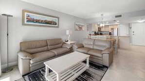 Una sala de estar moderna con un sofá color beige, una mesa de centro blanca y un cuadro de una escena costera.