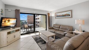 Una sala de estar moderna con sofá, mesa de centro, televisor y un balcón con mesa y sillas.