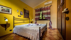 A bedroom with a bed, a nightstand, a wall-mounted shelf, a window with curtains, and a door with a handle.