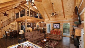 A spacious log cabin with a high ceiling, a dining area, a living room with sofas, a foosball table, and a balcony with a view. - Moose-n Around: Cut Loose in the Smokies (Sevierville)