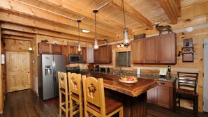 A wooden cabin-style kitchen with a central island, wooden chairs, a refrigerator, a microwave, and a sink. - Moose-n Around: Cut Loose in the Smokies (Sevierville)