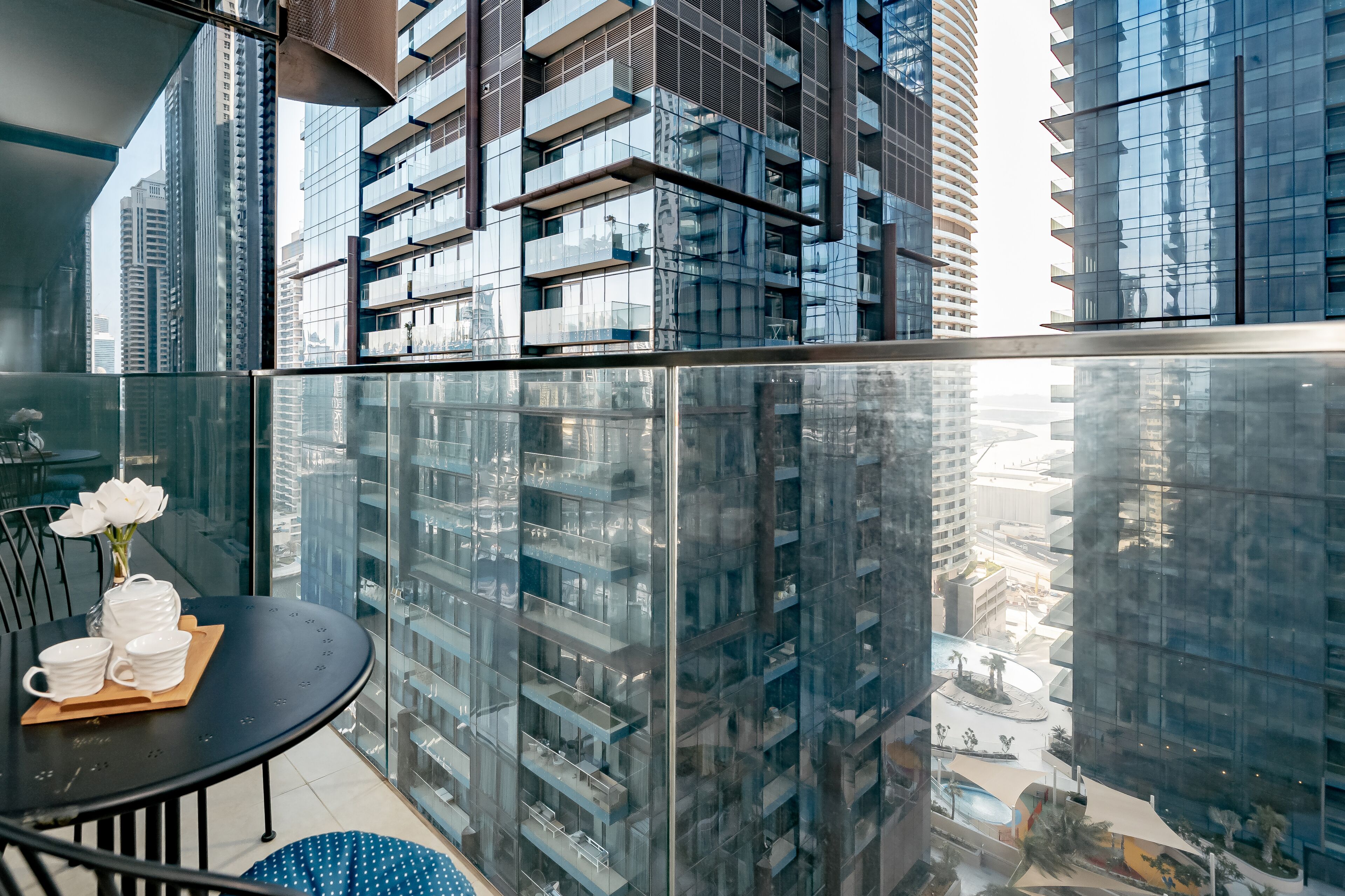 A modern high-rise building with reflective glass windows, a balcony with a table set for two, and a vase with white flowers.