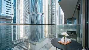 A balcony with a table set for two, overlooking a cityscape with high-rise buildings. - HiGuests - Marina Gate Tower (Dubai)