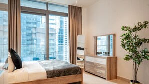 A modern bedroom with a large bed, a dresser, a mirror, and a potted plant. - HiGuests - Marina Gate Tower (Dubai)