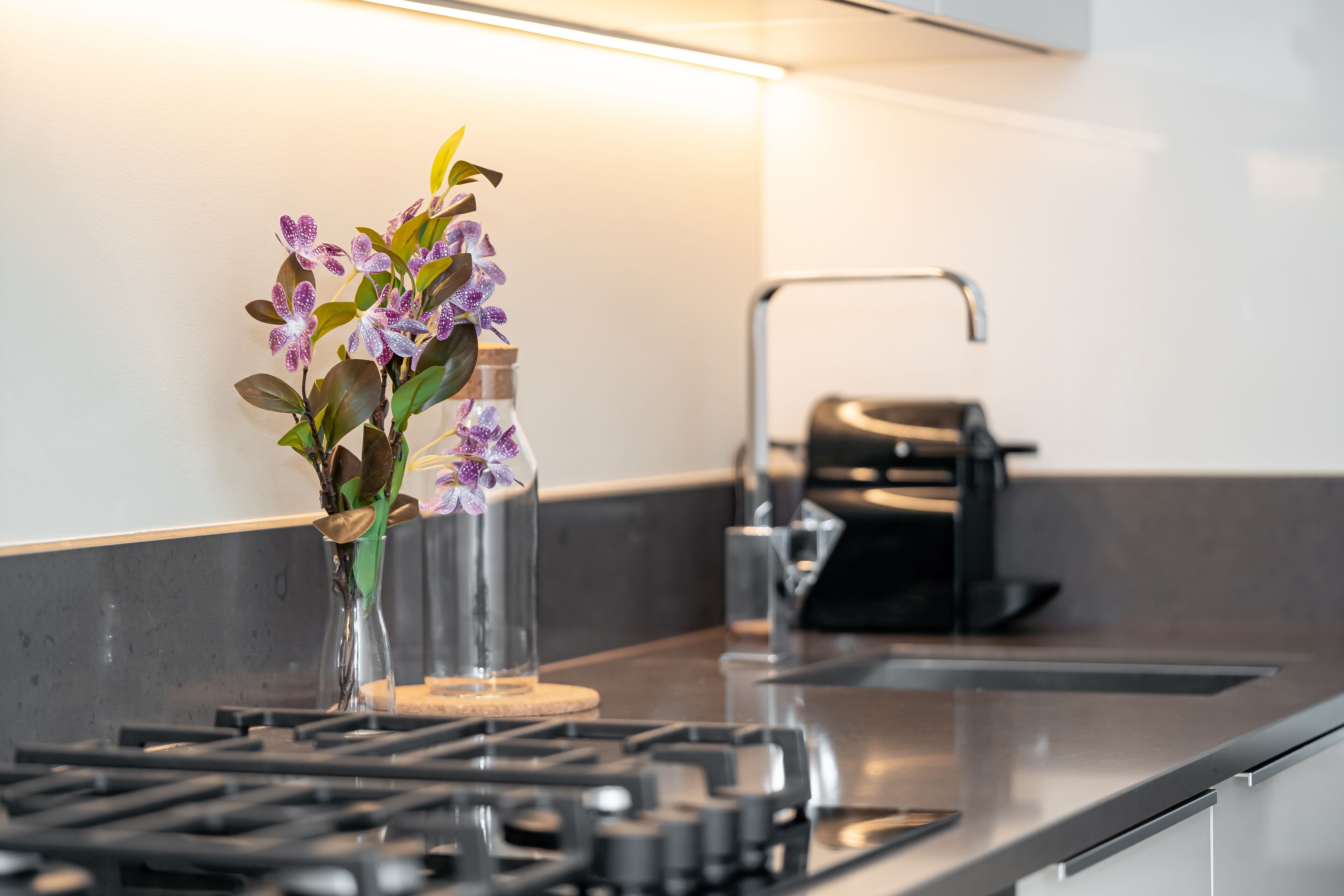 A kitchen with a gas stove, a sink, and a vase with flowers on the countertop.