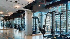 A gym with exercise equipment, large windows, and a city view. - HiGuests - Marina Gate Tower (Dubai)