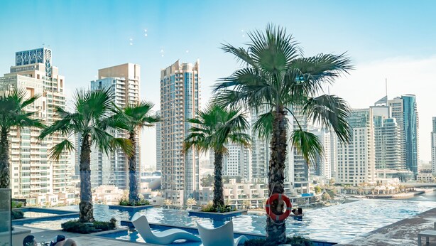 A poolside area with palm trees, lounge chairs, and a view of high-rise buildings. - HiGuests - Marina Gate Tower (Dubai)