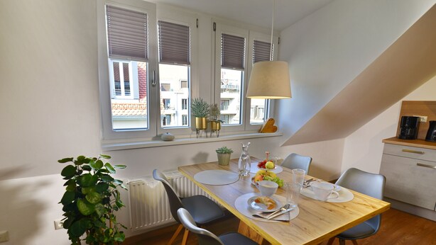 A dining area with a wooden table, four chairs, a potted plant, and a window with blinds.