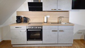 A compact kitchen with a built-in oven, a coffee maker, a sink, and a flat-screen TV mounted above the cabinets.