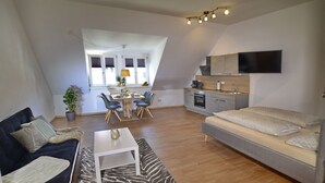 A modern apartment with a dining area, kitchenette, and a living room with a sofa and a bed.