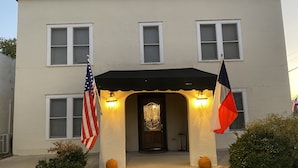 A two-story building with a black awning over the entrance, two flags, and two pumpkins on the steps.