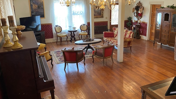 A spacious living room with a grand piano, multiple seating areas, and a large chandelier.