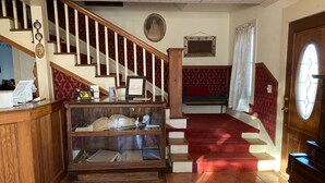 A staircase with a wooden handrail and red carpet, leading to a room with a wooden desk and a glass display case.