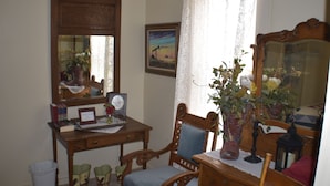 A room with a wooden desk, a chair, a mirror, and a vase with flowers.