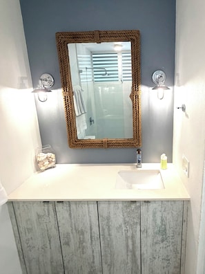Een badkamer met een houten wastafelmeubel, een spiegel met een touwlijst en een witte wasbak.