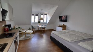 A modern bedroom with a large bed, a desk, and a kitchenette.