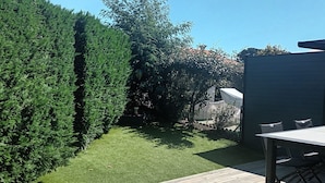 A wooden deck with a table and chairs, surrounded by a well-maintained lawn and a tall hedge. - Rental with heated swimming pool 800m from the sea  (Brem-sur-Mer)