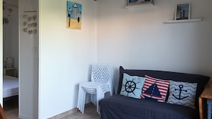 A cozy living room with a dark sofa, a round coffee table, and nautical-themed cushions. There is a white chair and a small white shelf with pictures. - Rental with heated swimming pool 800m from the sea  (Brem-sur-Mer)