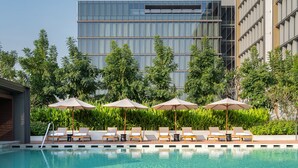 A modern hotel pool area with lounge chairs and umbrellas, surrounded by greenery and a contemporary building. - Hyatt Regency Phnom Penh (Phnom Penh)