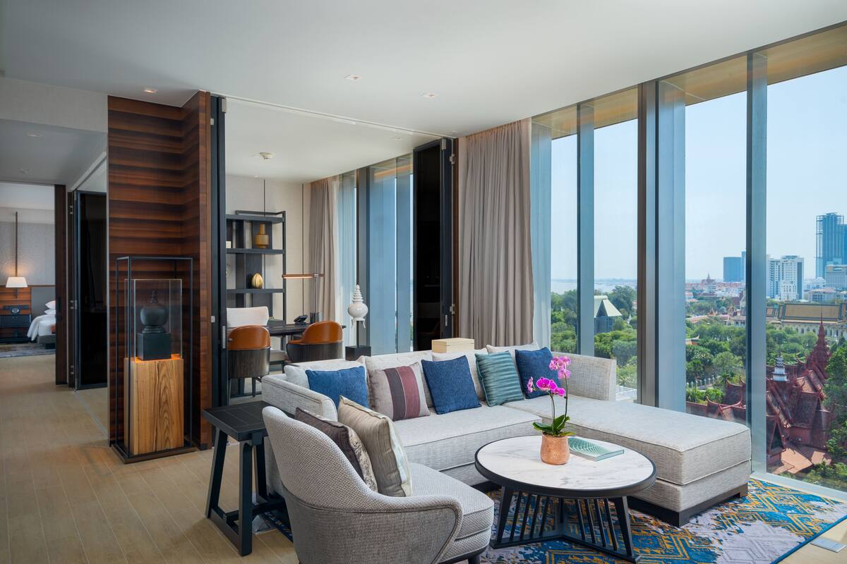 A modern living room with a sofa, chairs, and a coffee table. There is a large window with a city view.