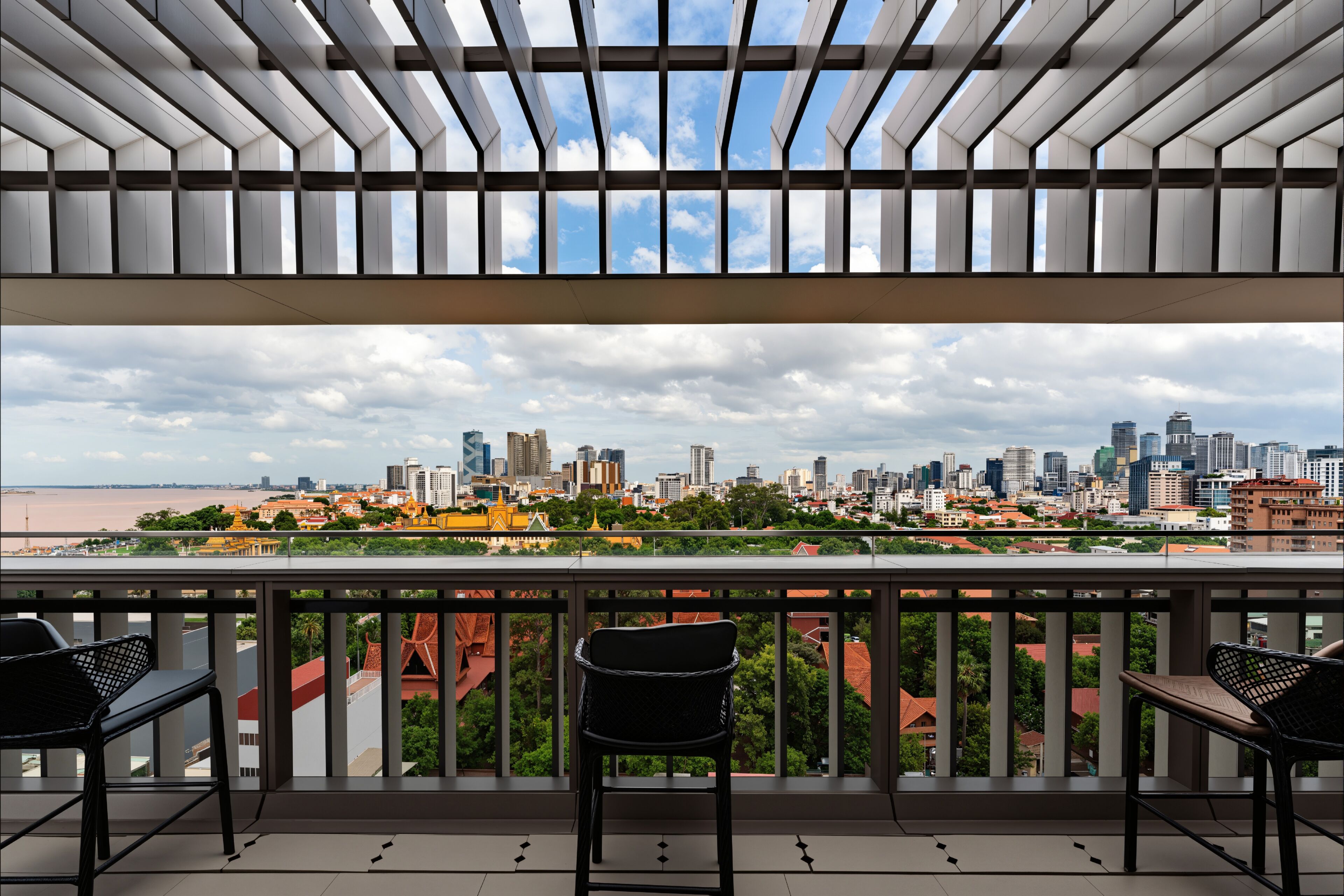 A balcony with a view of a city skyline, two chairs, and a railing.