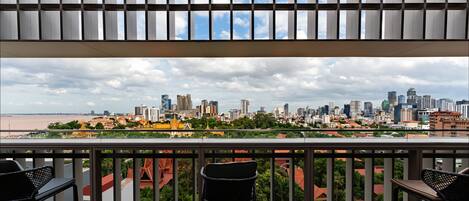 A balcony with a view of a city skyline, two chairs, and a railing.