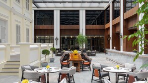 A spacious outdoor seating area with multiple tables and chairs, surrounded by large windows and a modern architectural design. - Hyatt Regency Phnom Penh (Phnom Penh)