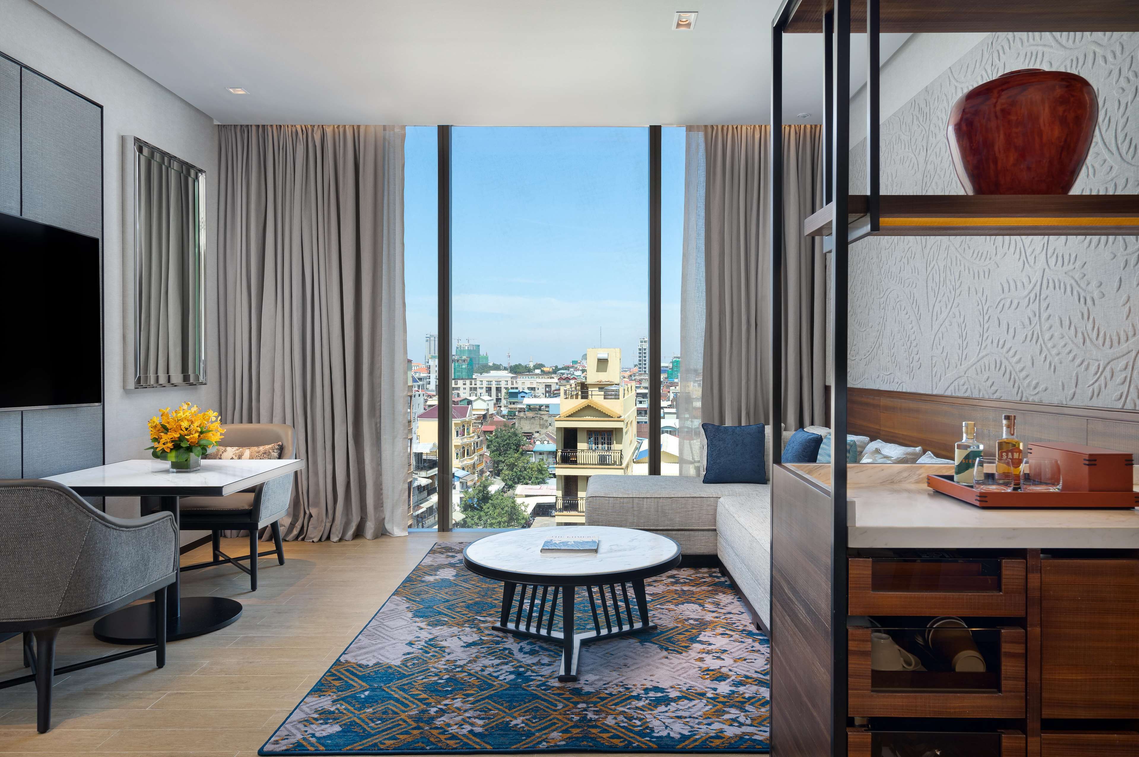 Une chambre d’hôtel moderne dotée d’une grande fenêtre, d’un coin repas, d’un canapé et d’un téléviseur fixé au mur.