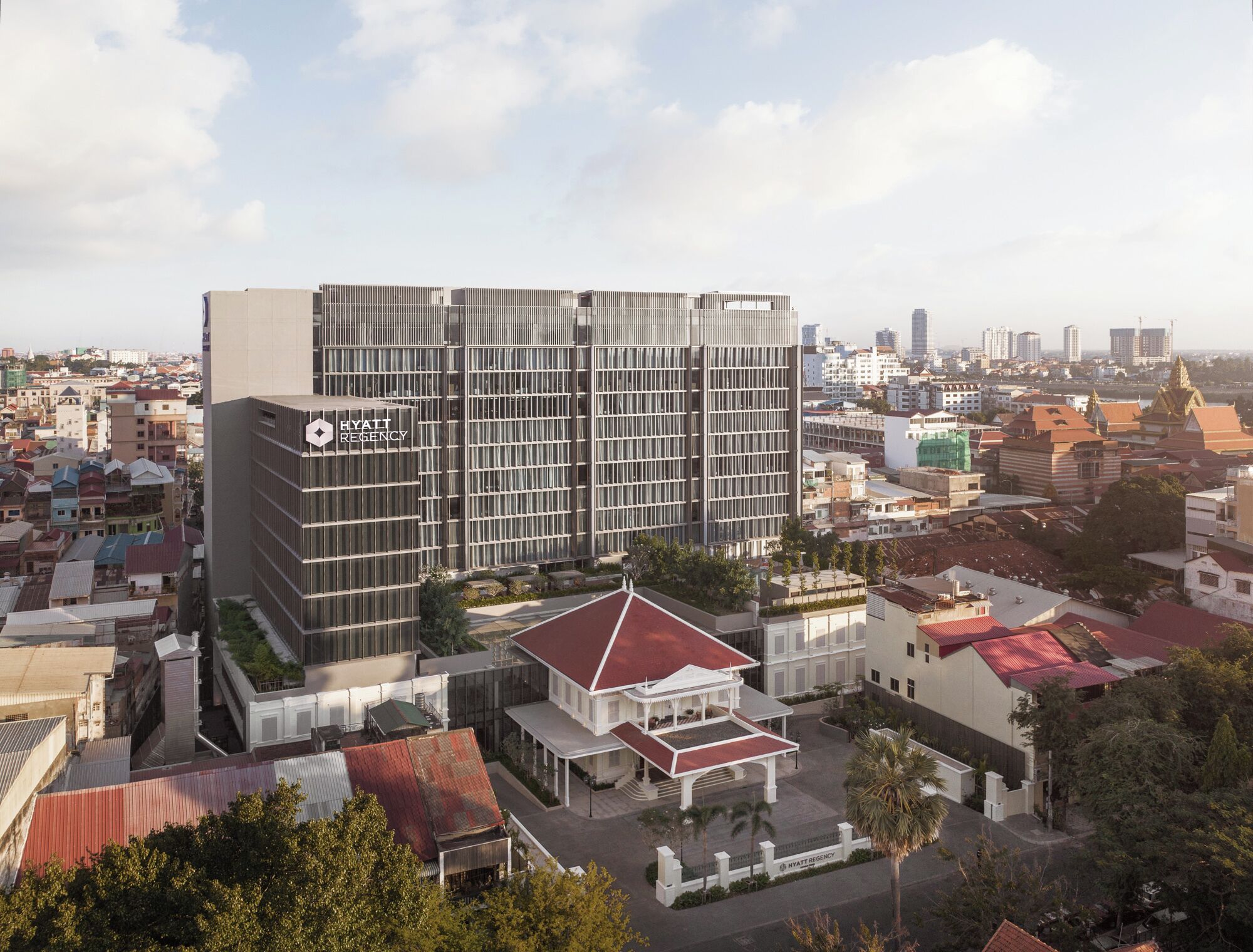 A modern hotel with a glass facade, a central courtyard, and a traditional building with a red roof.