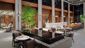 A modern indoor dining area with a central bar, multiple seating arrangements, and large windows. - Hyatt Regency Phnom Penh (Phnom Penh)