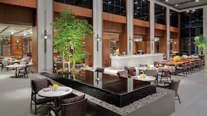 A modern indoor dining area with a central bar, multiple seating arrangements, and large windows. - Hyatt Regency Phnom Penh (Phnom Penh)