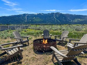 A fire pit with four Adirondack chairs arranged around it, set against a backdrop of a mountainous landscape. - Amazing Tamarack Resort Views, Hot Tub, Huge Lot! (Donnelly)