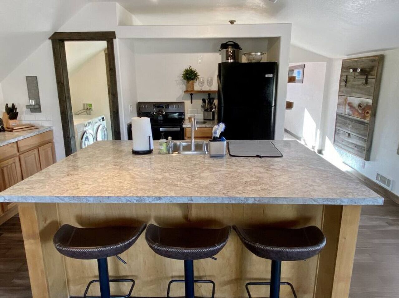 Una cocina con una isla grande, taburetes de bar, un refrigerador y una estufa.