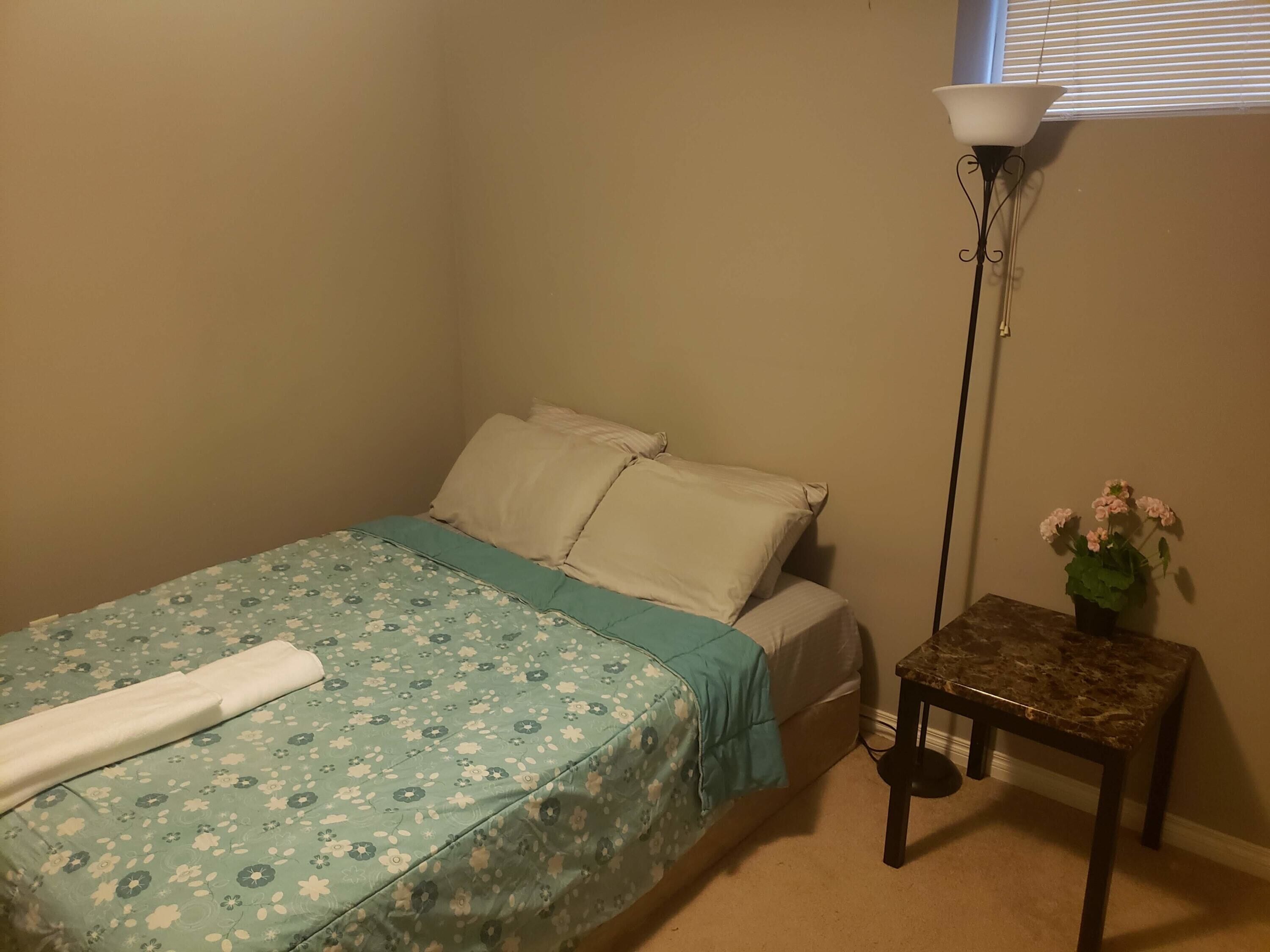 Une chambre à coucher avec un lit, une table de chevet ornée d’une plante et une lampe sur pied.