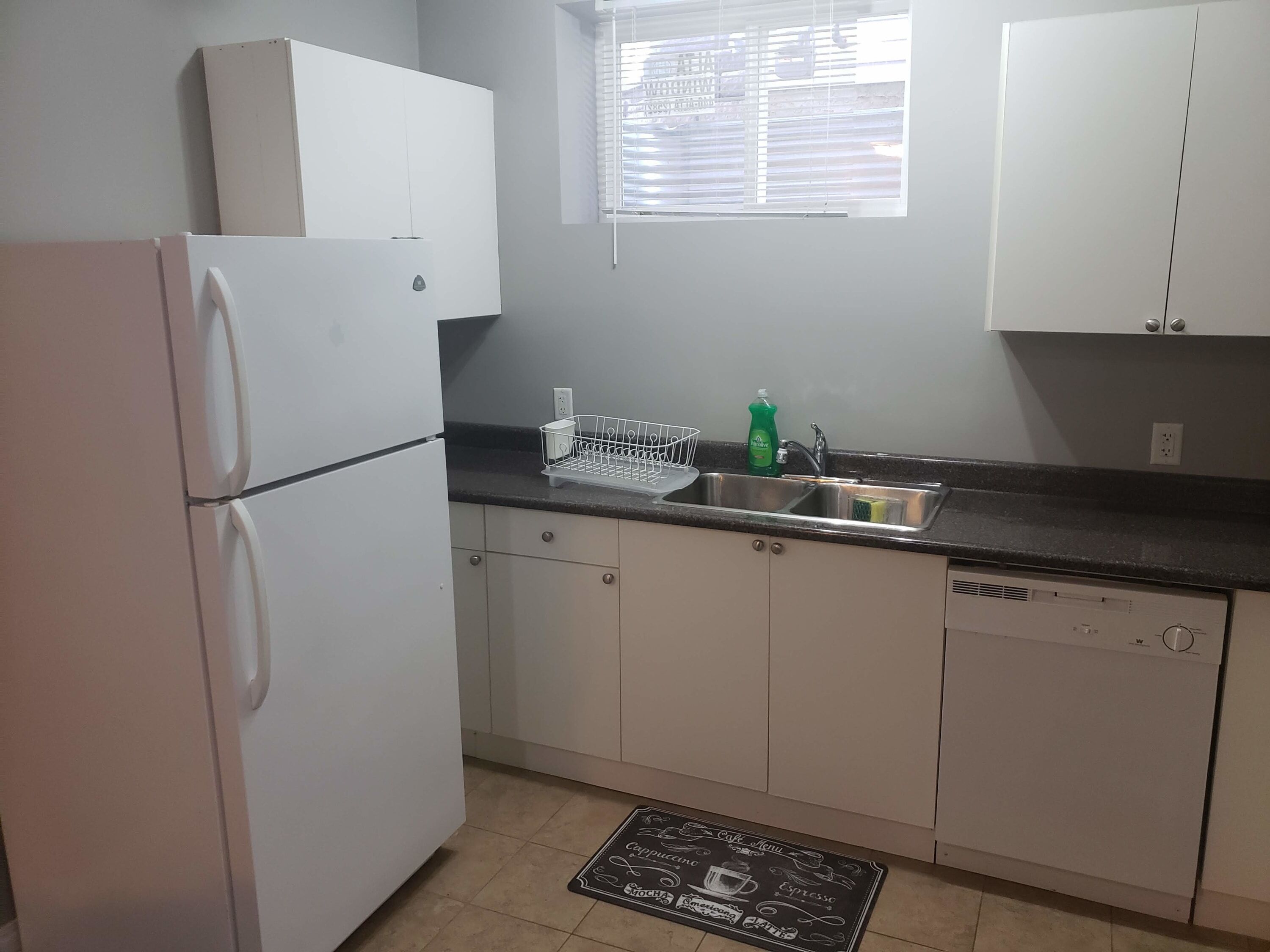 A compact kitchen with white cabinets, a stainless steel sink, and a dish rack.
