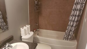 A bathroom with a sink, toilet, and bathtub. There are three rolls of toilet paper on the toilet.