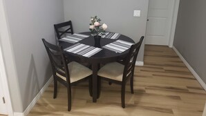 A dining area with a round table, four chairs, a vase with flowers, and three framed pictures on the wall.